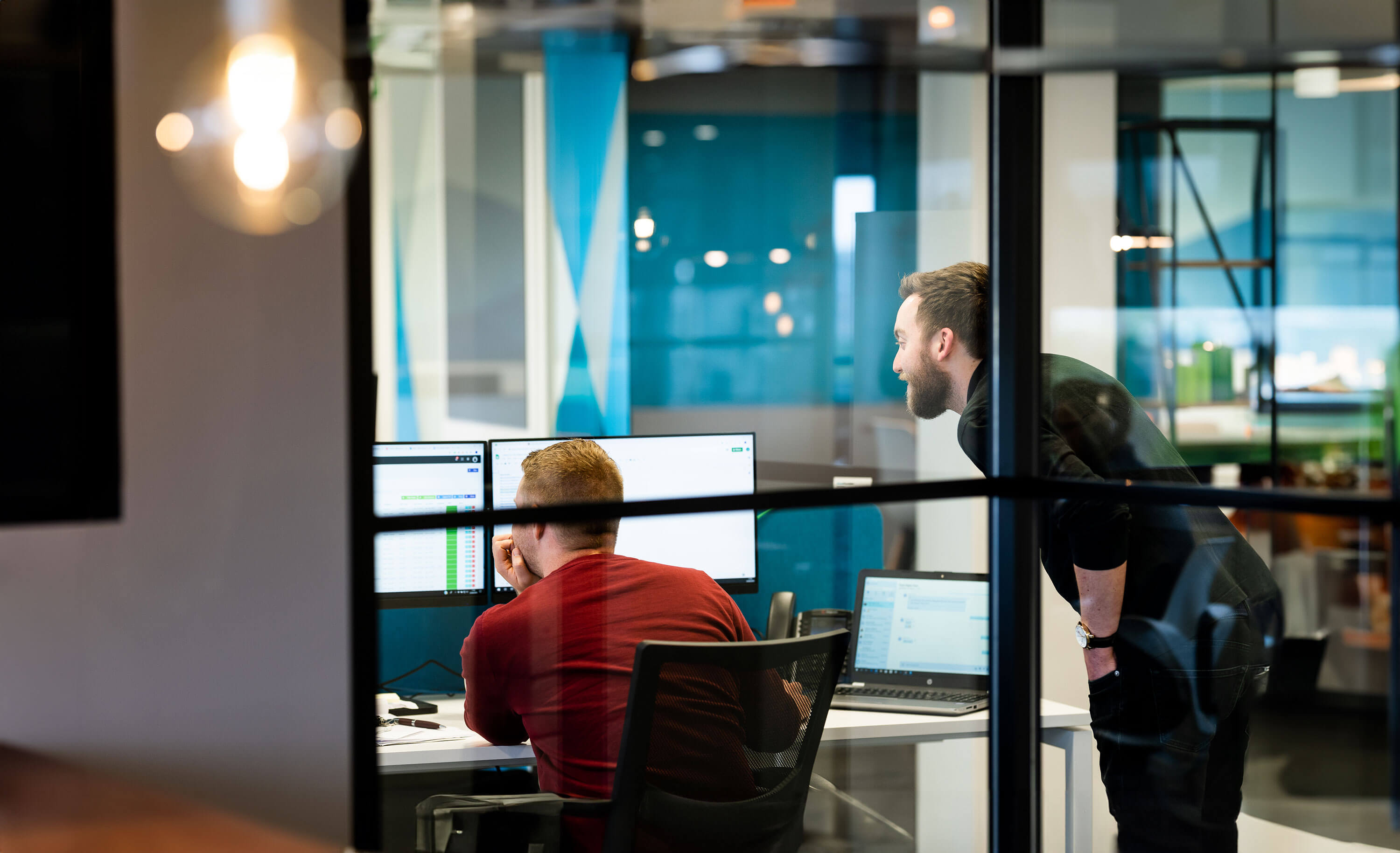 Resolute Cyber team members collaborating and reviewing data on dual monitors in a glass-walled office room.